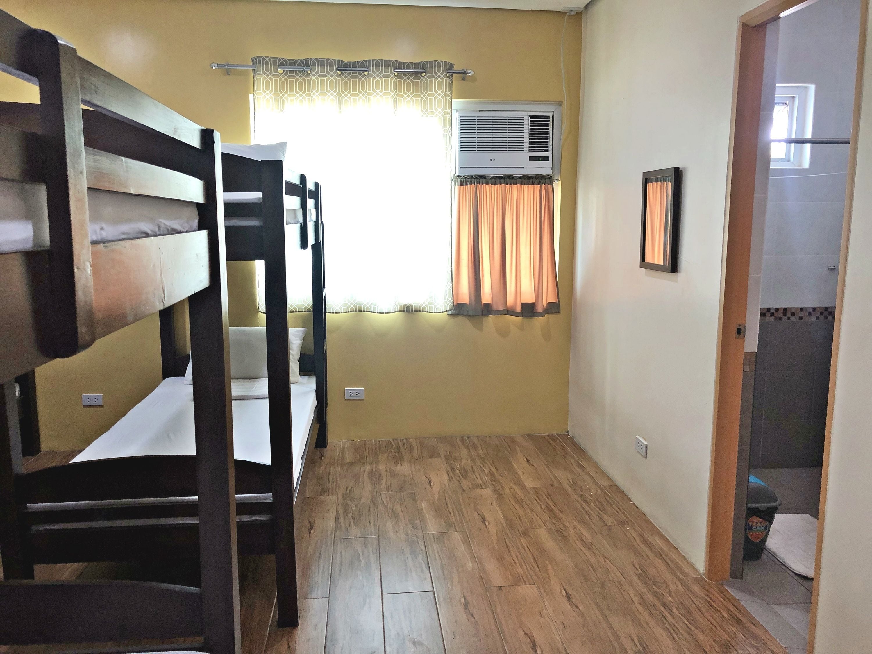 A room with bunk beds, an air conditioning unit, a window with curtains, and a door leading to a bathroom.