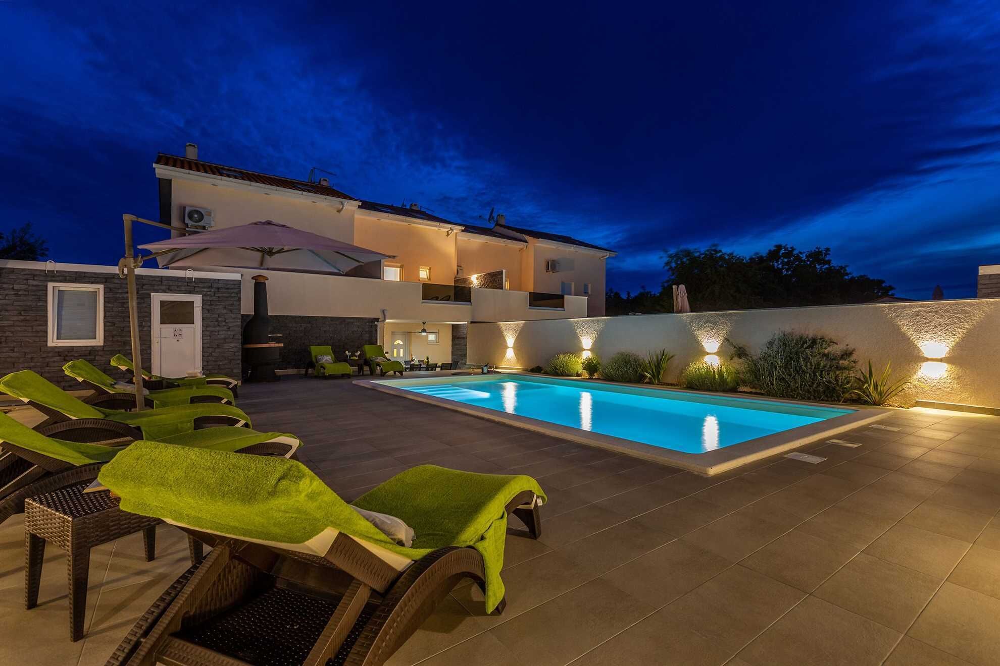 Un área de piscina exterior moderna con sillones de descanso y una parrilla.