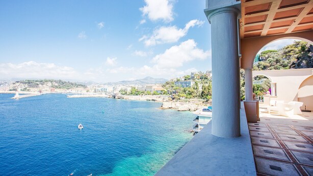 A seaside view from a balcony with a clear blue sea, a distant cityscape, and a rocky coastline. - LE CAP DE NICE VI4150 by RIVIERA HOLIDAY HOMES (Niza)