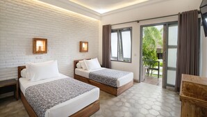 Habitación de hotel con dos camas, pared de ladrillo blanco y un amplio ventanal corredero que da a un espacio al aire libre.