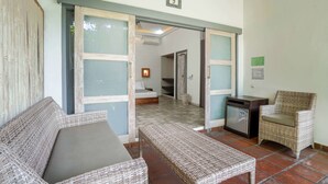 Habitación con muebles de mimbre, una pequeña kitchenette y vista a otra habitación con cama y un cuadro en la pared.