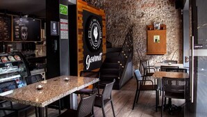 En café med en rustik murstensvæg, et skilt der står 'Gourmet', og en trappe, der fører op til en etage.