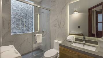 Een moderne badkamer met een glazen douchecabine, een marmeren betegelde wand, een wastafel met spiegel en een toilet.