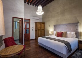 Een slaapkamer met een groot bed, een houten garderobe, een rode fauteuil en een houten tafel.