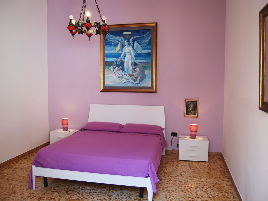 Een slaapkamer met een bed, twee nachtkastjes, een kroonluchter, een schilderij en een lijst met een foto aan de muur.