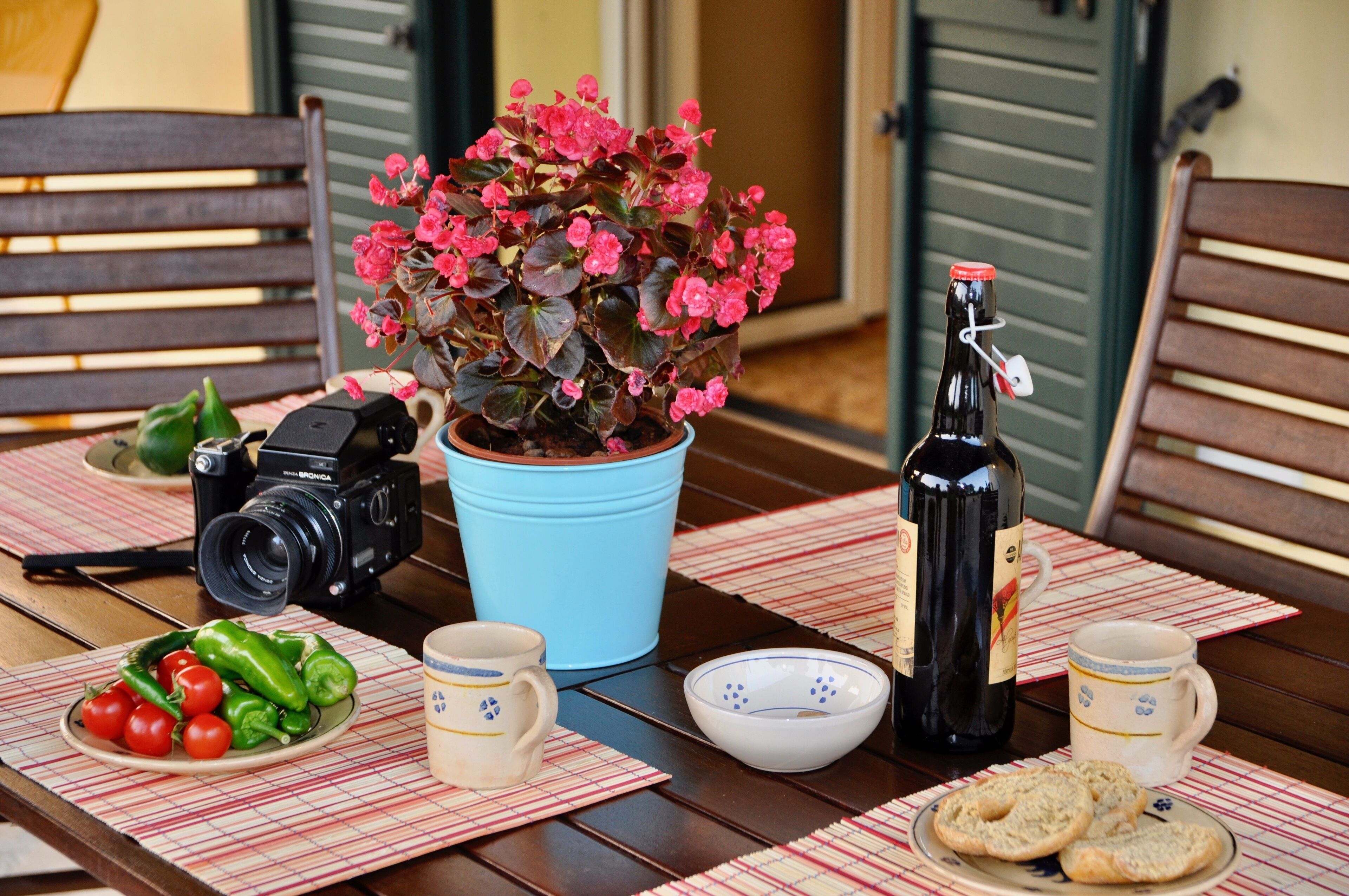A dining table with a camera, a potted plant, a bottle, and food items.