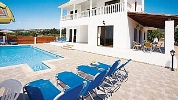 A two-story building with a swimming pool, blue lounge chairs, and a covered patio area. - Stunning 4 Bedroom Villa -Private Pool - Sea View (Peyia)