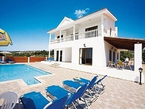 Un edificio de dos pisos con piscina, sillas de descanso azules y un patio cubierto.