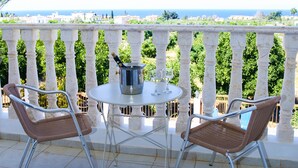 A balcony with two wicker chairs and a small table, a bottle of champagne, and a glass. - Stunning 4 Bedroom Villa -Private Pool - Sea View (Peyia)