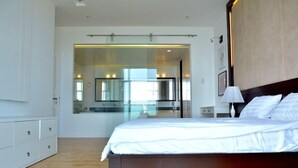 Un dormitorio moderno con una cama grande, una mesita de noche con lámpara, un armario y una puerta de cristal que da al baño.