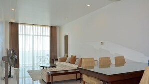Amplia sala de estar con una gran mesa de comedor de vidrio, sofás color beige y un ventilador de pie.