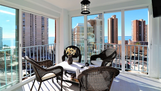 A balcony with wicker furniture, a vase with flowers, and a hanging light fixture. - Ocean II 9-C (Benidorm)