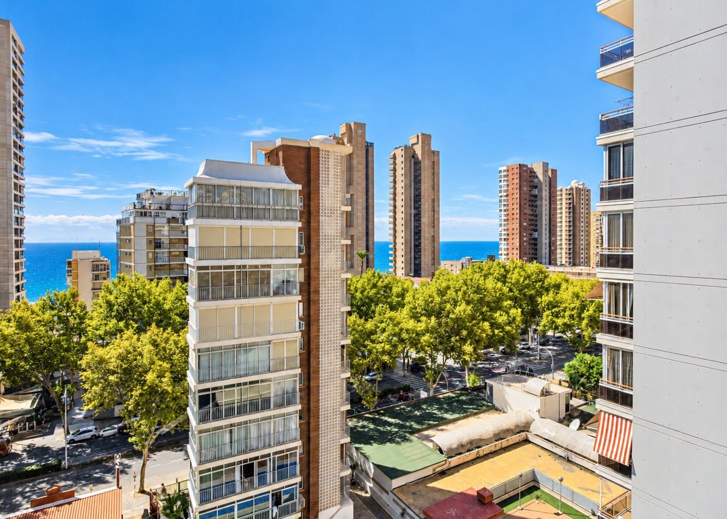 A high-rise residential building with multiple balconies, a rooftop terrace, and a view of the sea.