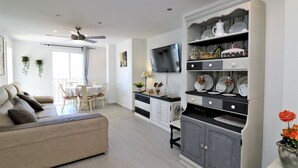 A modern living room with a sofa, dining table, and kitchen area with cabinets and a TV. - Ocean II 9-C (Benidorm)