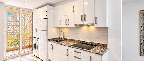 Una cocina moderna con armarios blancos, encimera de granito, horno empotrado y lavadora.