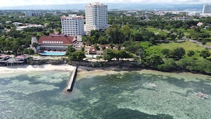 An aerial view of a coastal hotel with a beach, clear waters, and a pier. - Lux. 2BR condo + 2 pools, woow oceanviews, Gym, Beach,near Mactan Newtown, Tours (Lapu-Lapu City)