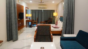 A hotel room with a bed, a sofa, a desk with a lamp, a chair, and a television.