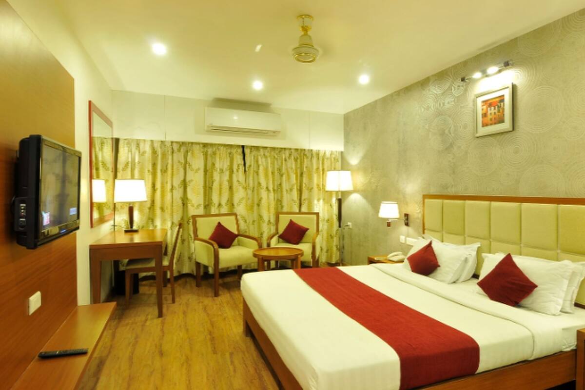 A hotel room with a large bed, two chairs, a TV, and a desk.