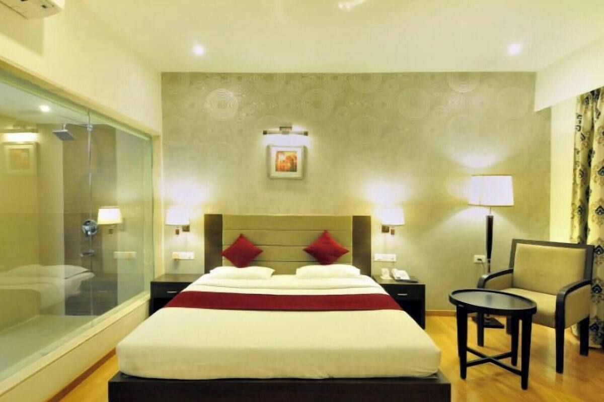 A hotel room with a large bed, a glass shower enclosure, a chair, and a small table.