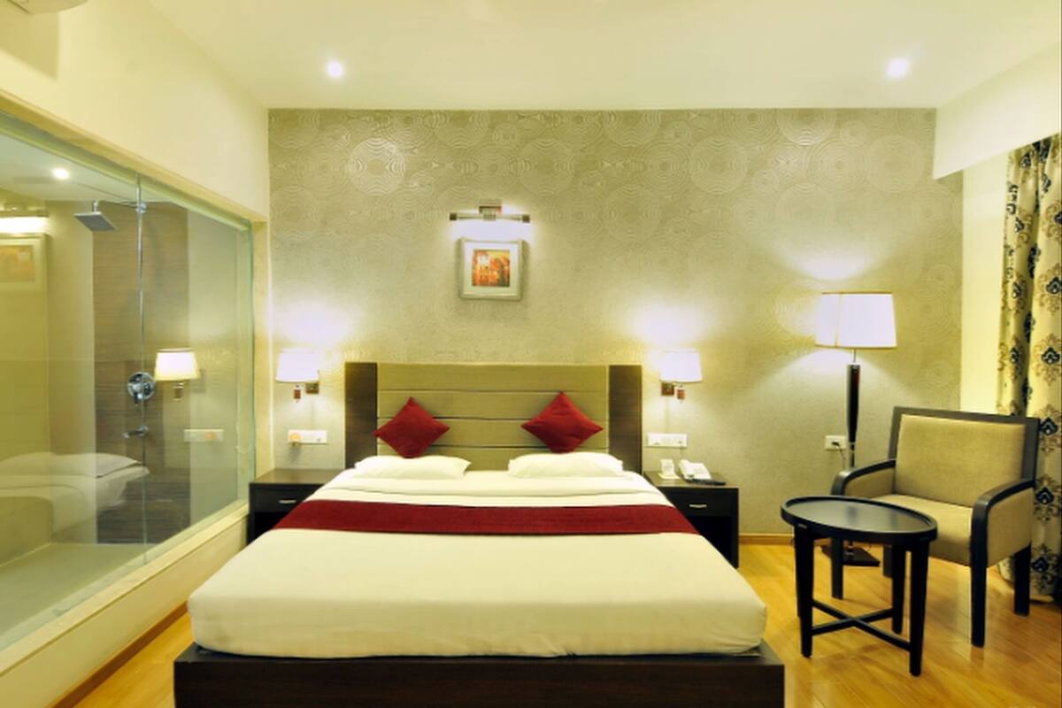 A hotel room with a bed, bedside tables, a chair, a desk, and a glass shower enclosure.