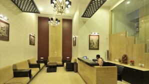 A reception area with a wooden reception desk, beige sofas, a chandelier, and framed artwork on the walls.
