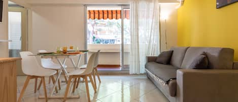 A modern living room with a sofa, dining table, chairs, and a window with curtains.