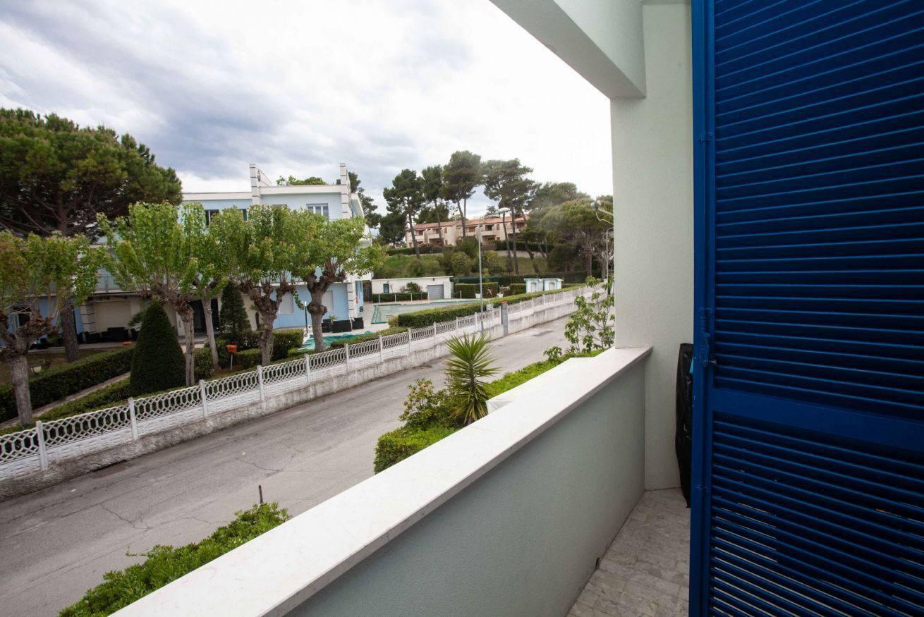 Ein Balkon mit Blick auf eine Straße, einen weißen Zaun und Bäume.