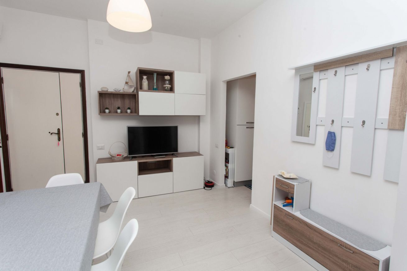 A modern living room with a dining table, white chairs, a flat-screen TV, built-in shelves, and a wooden cabinet.