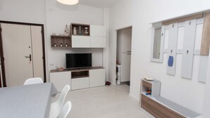 Ein modernes Wohnzimmer mit Esstisch, weißen Stühlen, einem Flachbildfernseher, Einbauschränken und einem Holzkabinett.