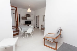 Un espacio habitable moderno y abierto con comedor, televisor y zona de estar con una silla.