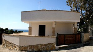 Uma casa moderna, térrea, com telhado plano, alicerce de pedra e portão de madeira.