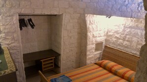 Ein kleiner Raum mit Steinwänden, ausgestattet mit einem Bett, einer Bank und einem Schuhregal.