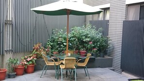 A patio with a glass table and chairs, surrounded by potted plants and a green umbrella. - Feng Chia Love Heart (Taichung)