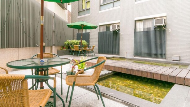 An outdoor patio with a small water feature, wicker chairs, a glass table, and an umbrella. - Feng Chia Love Heart (Taichung)