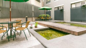 A courtyard with a small pond, a table with chairs, and a green umbrella. - Feng Chia Love Heart (Taichung)