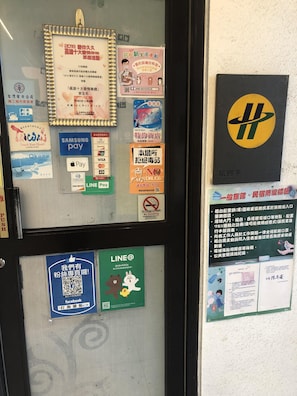 Un tablón de anuncios con varios avisos y calcomanías, incluyendo opciones de pago, un cartel de no fumar y un código QR de LINE.