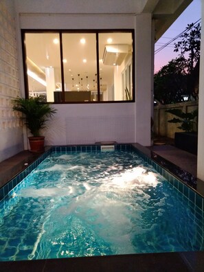 A hot tub with a view of a modern interior space, including a large window and indoor lighting. - Wee Hostel (Kanchanaburi)