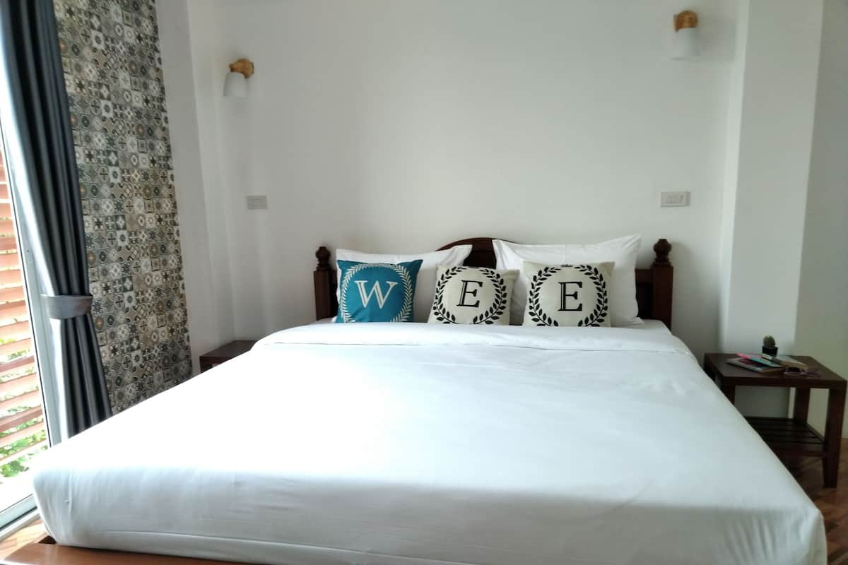 A neatly made bed with white bedding and three decorative pillows with the letters 'W', 'E', and 'E'.
