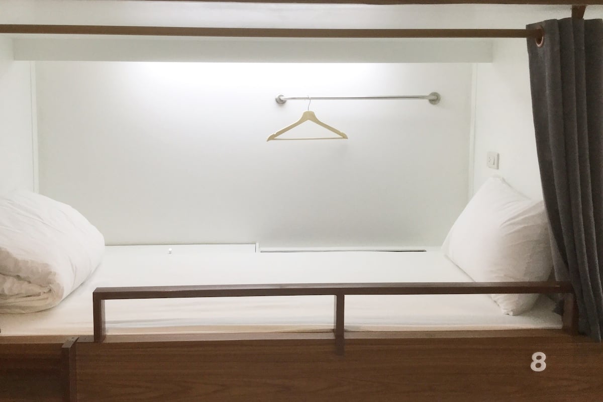 A single bed with a wooden frame, a white mattress, and a metal rod for hanging clothes.