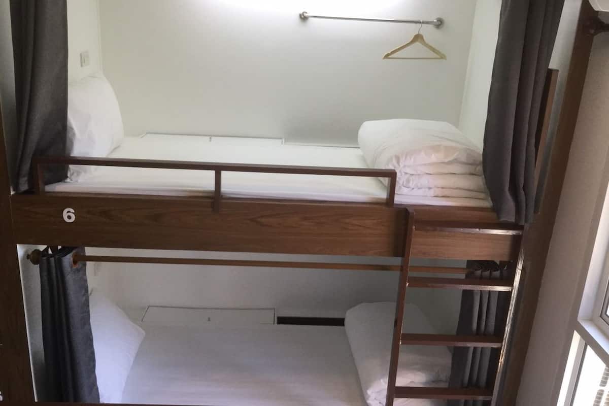 A bunk bed room with a wooden frame, a metal rod for hanging clothes, and a window with curtains.