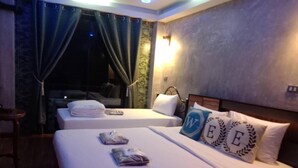 Une chambre d’hôtel avec deux lits, une petite table et une vue sur la ville la nuit.