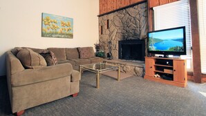 A living room with a stone fireplace, a television on a wooden stand, a sofa, and a painting on the wall. - Tahoe Olympic Condo | Carson Valley Views (Stateline)