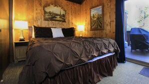 A bedroom with a large bed, wooden walls, two bedside lamps, and a painting above the bed. - Tahoe Olympic Condo | Carson Valley Views (Stateline)