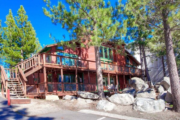 Una cabaña de madera de varios pisos con balcones, rodeada de grandes rocas y pinos.