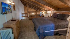 A cozy attic bedroom with a wooden ceiling, a large bed, a nightstand, a dresser, and a painting of a forest scene. - Tahoe Olympic Condo | Carson Valley Views (Stateline)