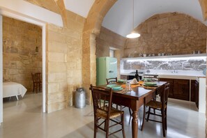 Cocina con paredes de piedra, una mesa de comedor para cuatro personas, un refrigerador de estilo antiguo y un lavabo con grifo moderno.