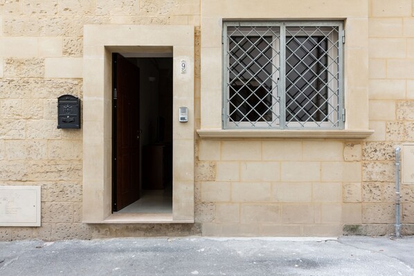 Un edificio color beige con una puerta y una ventana con barrotes.