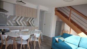 Une cuisine moderne avec un dosseret de carreaux disposés en motif chevron, un coin repas avec une table ronde et des chaises, et un canapé bleu agrémenté d’un coussin.