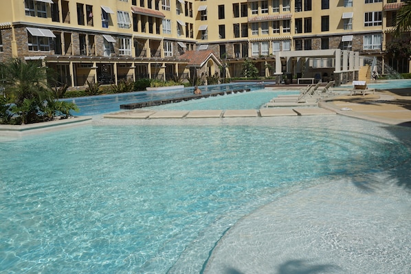 A resort pool area with clear water, surrounded by a building with balconies and a covered walkway.