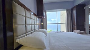 Quarto de hotel com uma cama grande, vista para o mar e uma janela com cortinas.